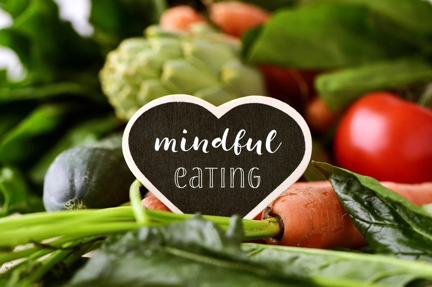 A heart-shaped sign reading mindful eating among fresh vegetables